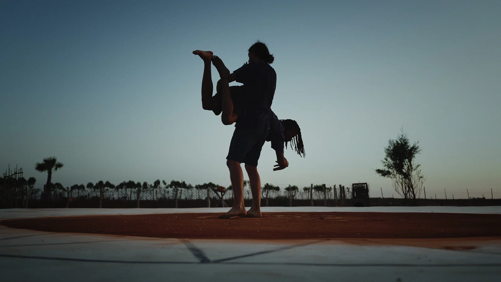 Two performers silhouetted in a lifting pose against a twilight sky, from Sacred Union (2022)
